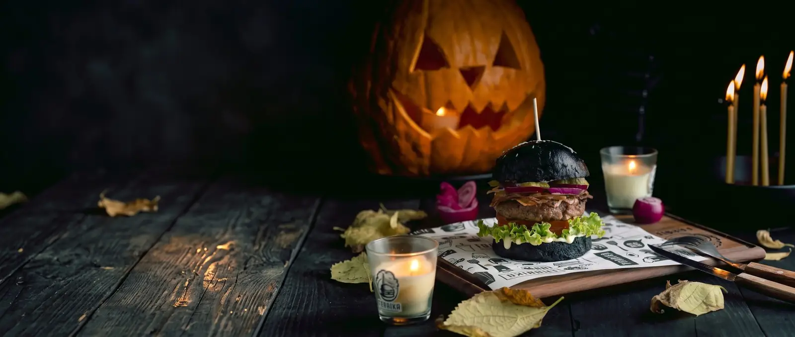 Burger u crnoj zemički pored izdubljene bundeve i sveća